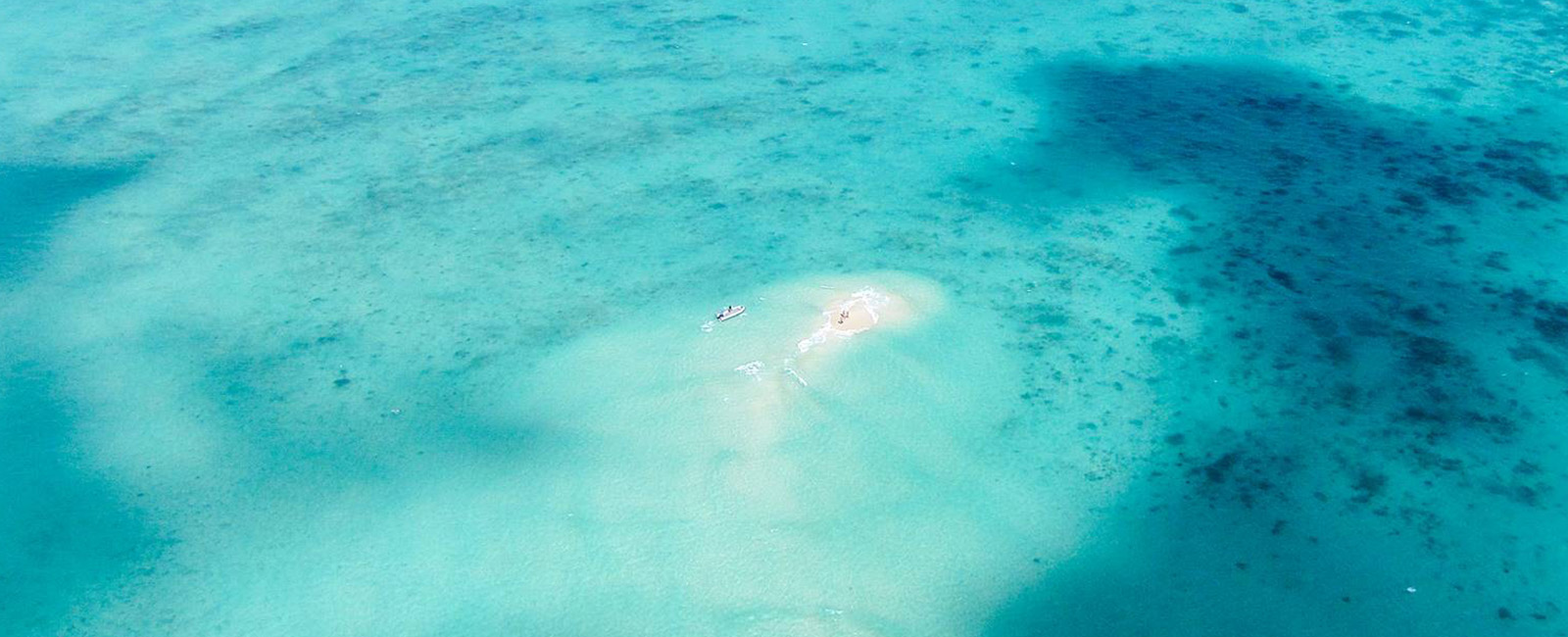 A small island and boat seen from above in sparkling blue seas 