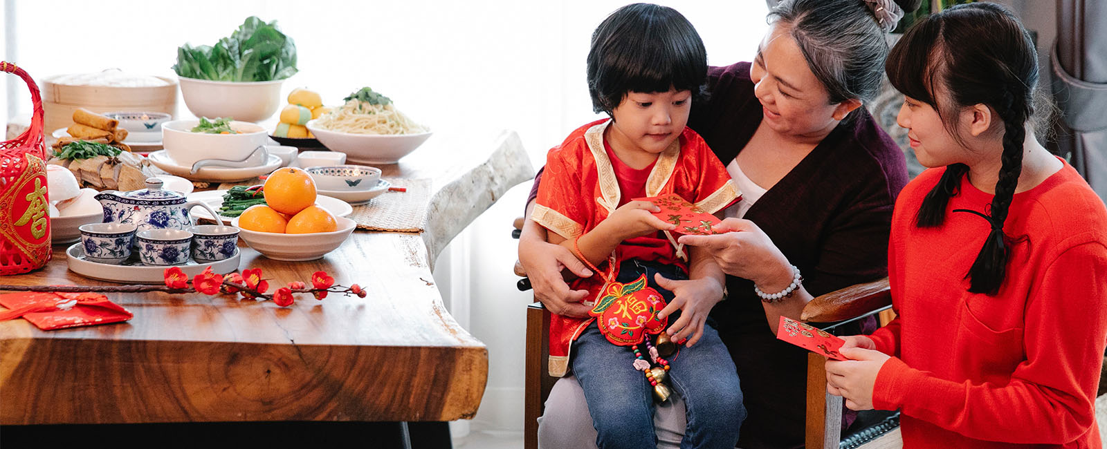 A chinese grandmother giving grandchildern red packets next to a table filled with different kinds of chinese food